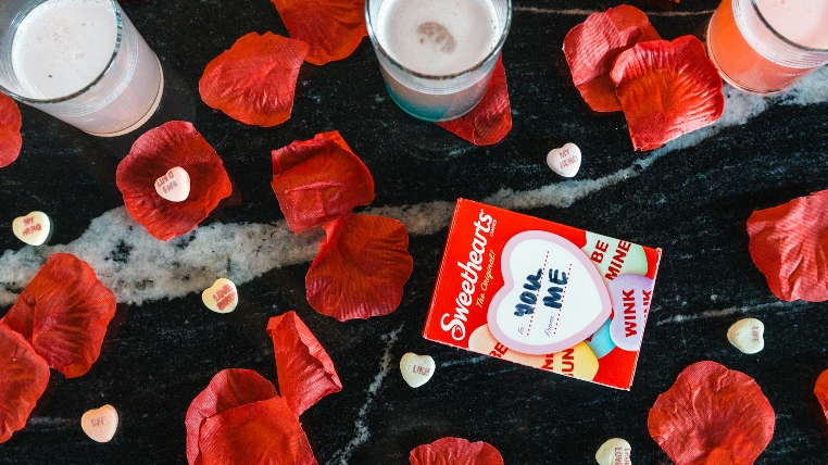 Sweethearts candy box on black surface with red petals and heart candies