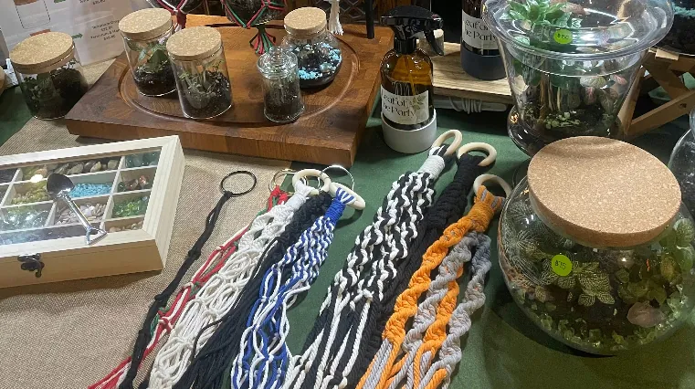 Assorted terrarium supplies including glass jars, macrame, spray bottle, glass orbs, and decorative rocks displayed on a table