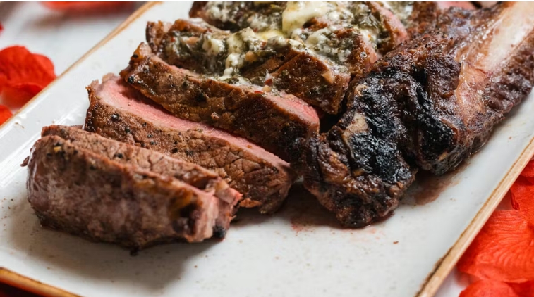 Slices of cooked steak with herb butter on a white plate