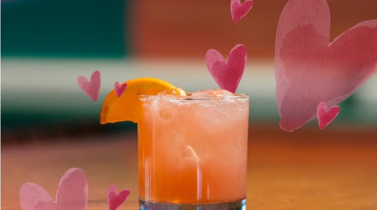 Cocktail garnished with orange slice, surrounded by pink hearts