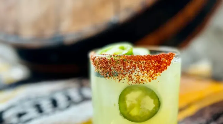 Cocktail with chili rim, jalapeño slices, wood barrel background