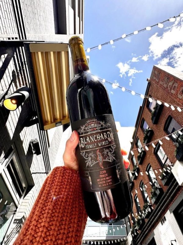 woman holding a blanchard family wines bottle to the sky in the alley at dairy block denver