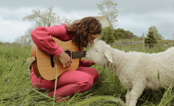 Sophia Eliana promo shot featuring her guitar and a sheep