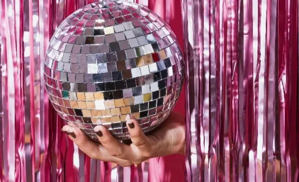 Hand holding a reflective disco ball against pink tinsel backdrop
