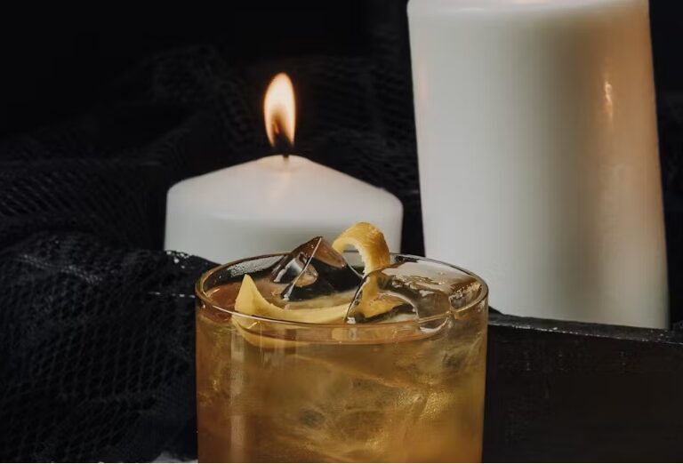 Whiskey cocktail with lemon twist, surrounded by lit white candles