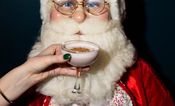 Santa Claus figure with eyeglasses, a hand offering a cocktail