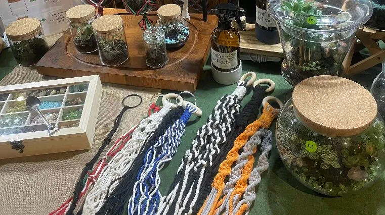 Assorted terrarium supplies including glass jars, macrame, spray bottle, glass orbs, and decorative rocks displayed on a table