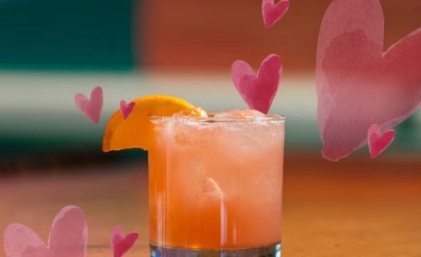 Cocktail garnished with orange slice, surrounded by pink hearts