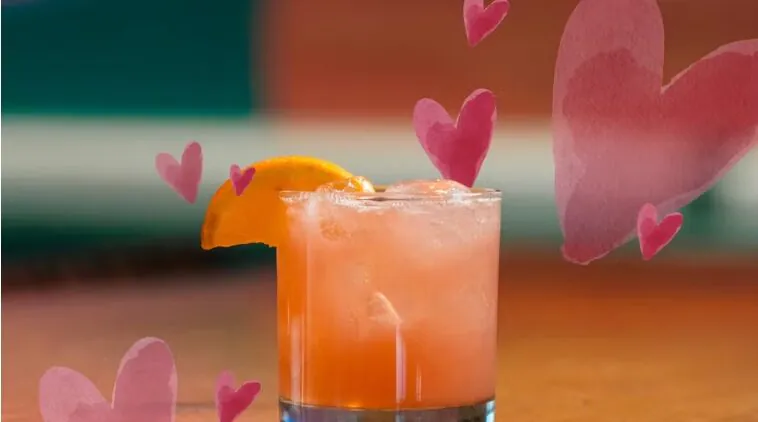 Cocktail garnished with orange slice, surrounded by pink hearts