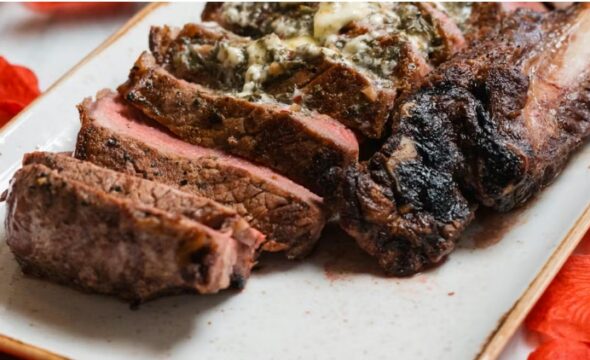 Slices of cooked steak with herb butter on a white plate